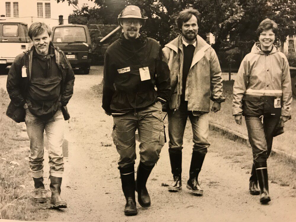 Neljä Saapas-päivystäjä kävelemässä saappaat jalassa. Kuva on seepianvärinen, 70-luvulta.