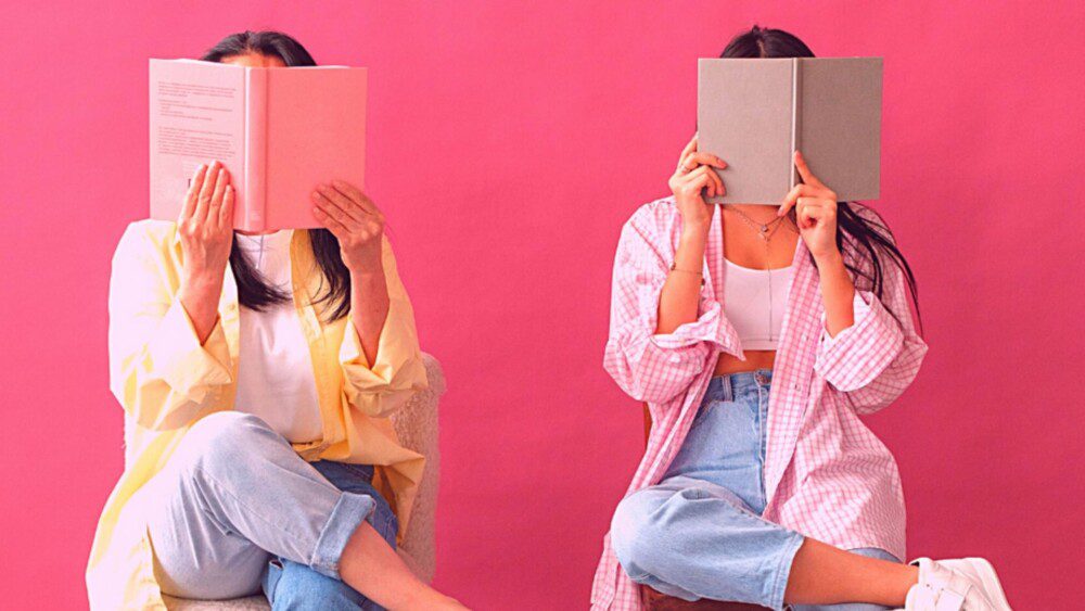 Kuvassa kaksi nuorta peittävät kasvonsa pitämällä kirjaa niiden edessä.