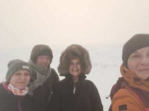 Neljä ihmistä ovat vierekkäin, he seisovat talvivaatteissa tunturin päällä.